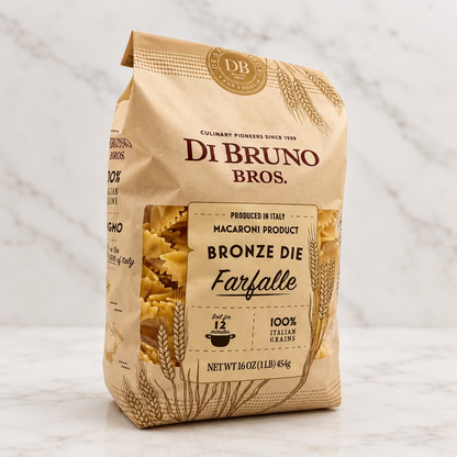 A 16 oz bag of Di Bruno Bros. Bronze Die Farfalle macaroni pasta, featuring a beige paper bag with brown text and wheat illustrations, set against a plain white studio background.