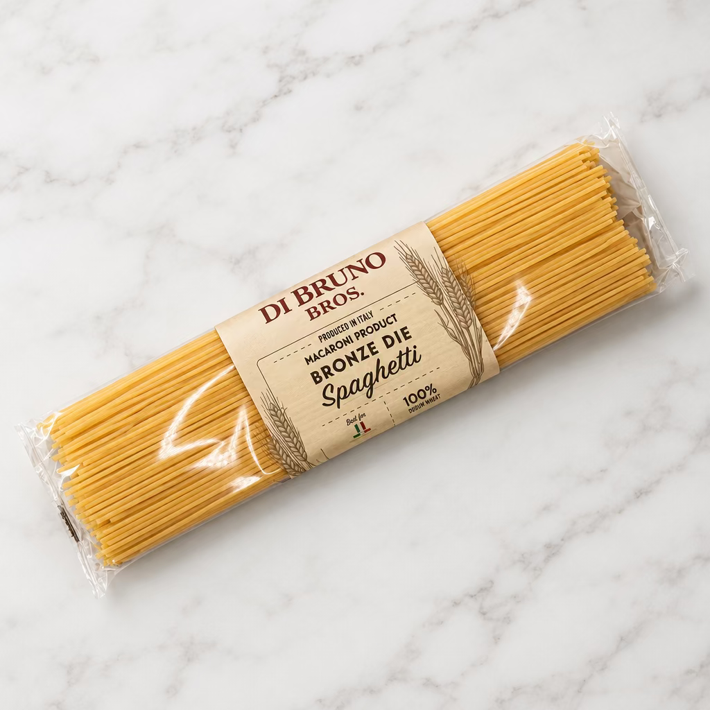 A package of Di Bruno Bros. Brownie Die Spaghetti, featuring uncooked spaghetti noodles in clear plastic wrapping with a tan paper label, placed on a white surface.