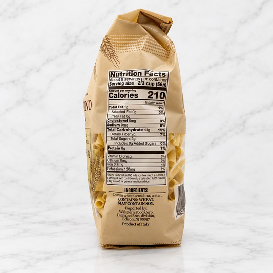 A bag of uncooked penne pasta shown from the back, displaying the nutrition facts label and ingredients against a plain white background.
