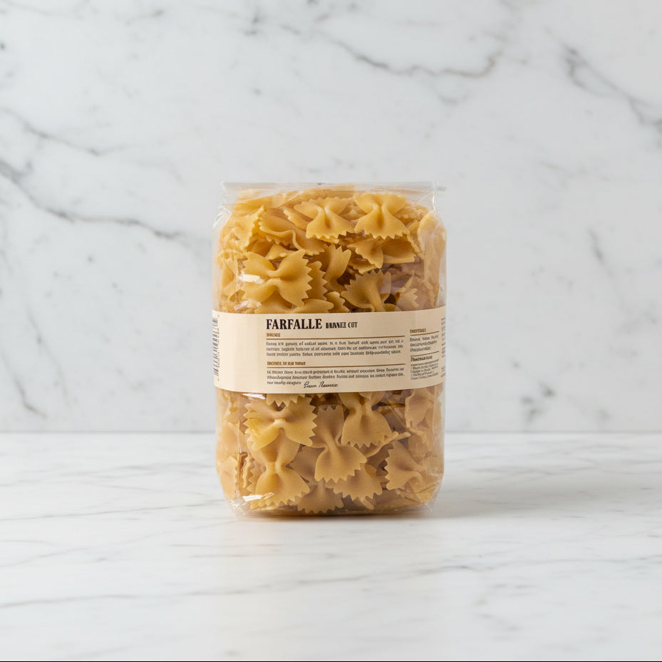 Bag of farfalle pasta on a white surface with a white box in the background