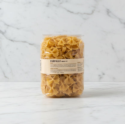 Bag of farfalle pasta on a white surface with a white box in the background