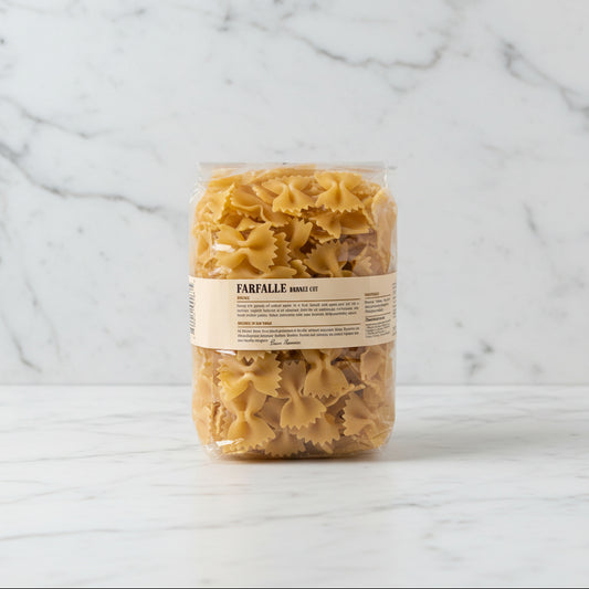 Bag of farfalle pasta on a white surface with a white box in the background