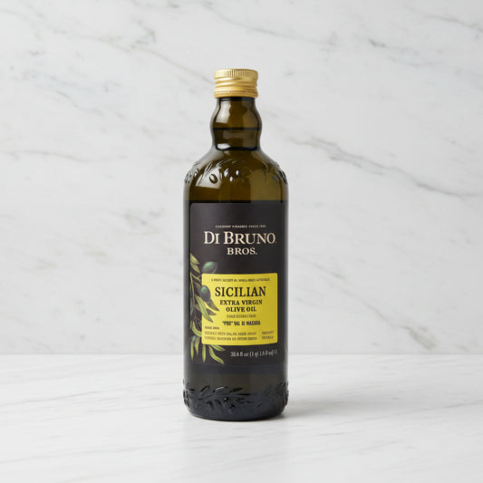 Bottle of Di Bruno Bros Sicilian Extra Virgin Olive Oil on a black surface with a warehouse background.