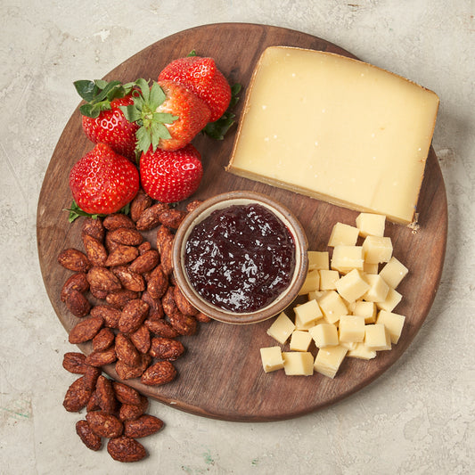 Wooden platter with strawberries, almonds, cheese, and jam on a light gray background