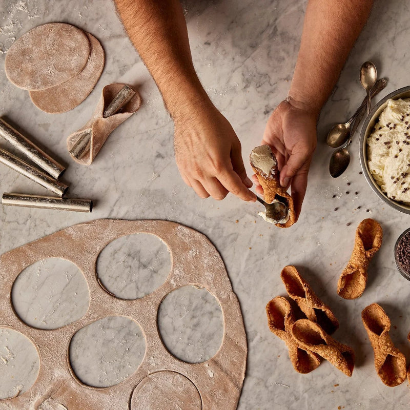 Person making cookies with various cookie cutters and ingredients on a concrete surface