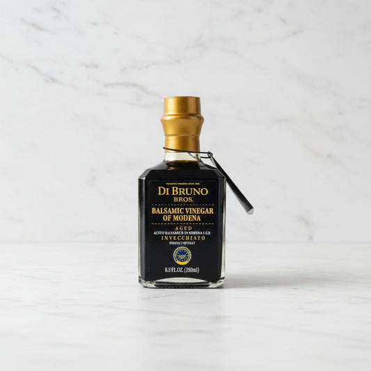 Bottle of Di Bruno Bros Balsamic Vinegar of Modena on a gray surface with a white tiled wall in the background.