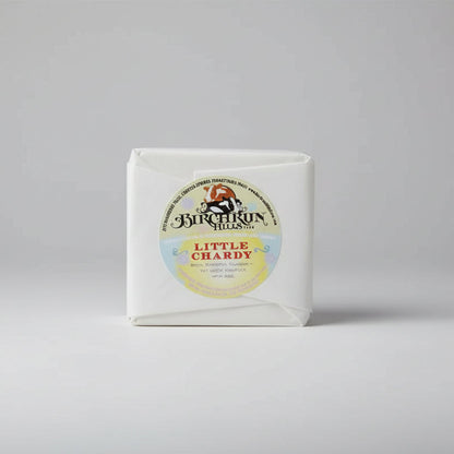 Block of cheese with 'Birchrun Hills' label on a wooden surface, with promotional material in the background.