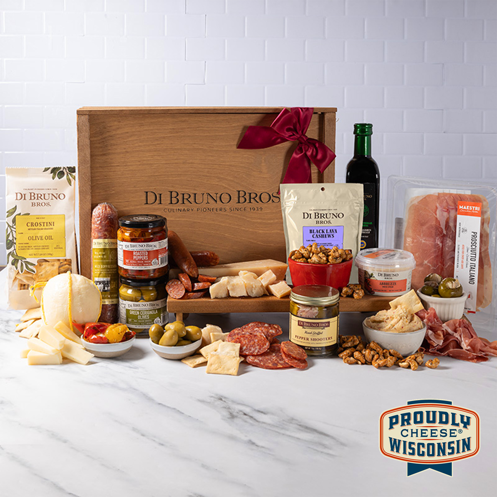 A gift crate from Di Bruno Bros. featuring an assortment of gourmet food items including pepperoni, candied nuts, provolone, prosciutto-stuffed pepper shooters, fire-roasted peppers, olives, balsamic vinegar, salami, cheese spread, crostini, and more.