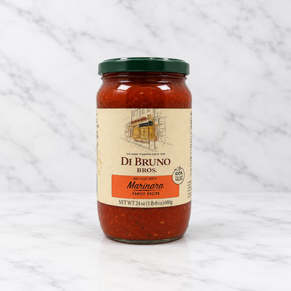 A glass jar of Di Bruno Bros. Marinara sauce with a cream label and a dark green lid, set against a white studio backdrop.