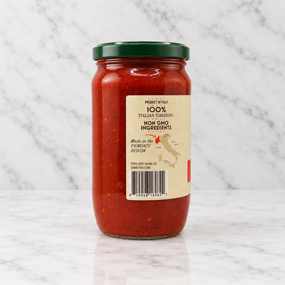 A glass jar of red sauce with a dark green lid and a cream-colored label, photographed against a plain white background.
