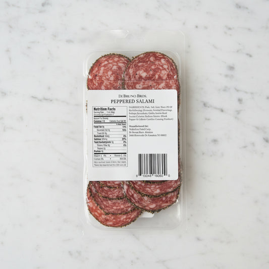 Packaged peppered salami with a label on a dark surface
