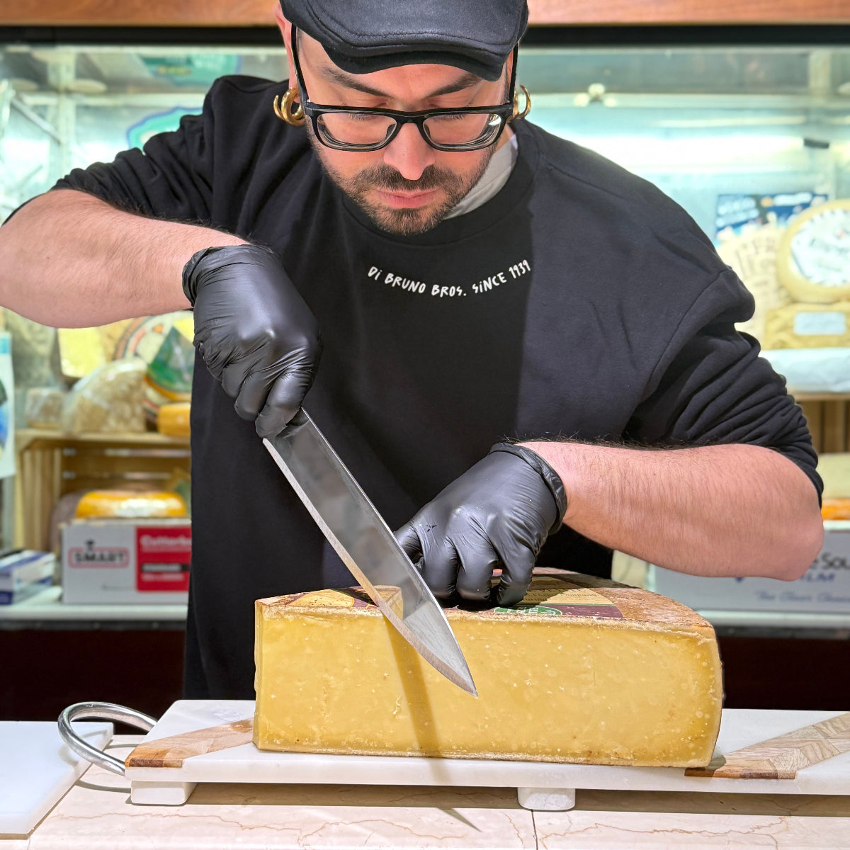 Tommy cutting cheese with a large knife in a store setting