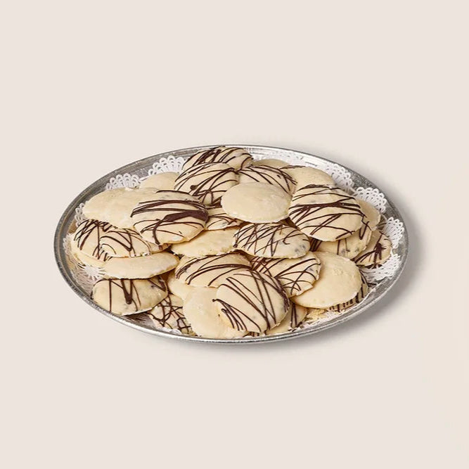 Decorative cookies with chocolate drizzle on a round plate against a beige background