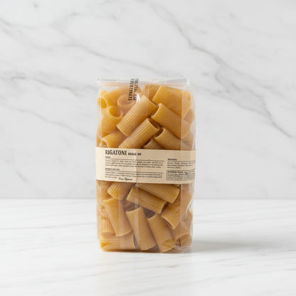 Bag of pasta with a label on a white surface, with a cardboard box in the background.