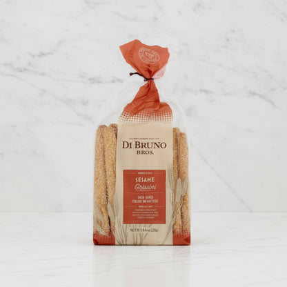 A bag of Di Bruno Bros. Sesame Grissini oven-baked Italian breadsticks in a clear plastic package with a beige and orange label, shown on a white background.