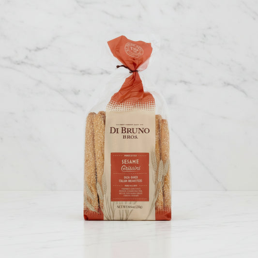 A bag of Di Bruno Bros. Sesame Grissini oven-baked Italian breadsticks in a clear plastic package with a beige and orange label, shown on a white background.