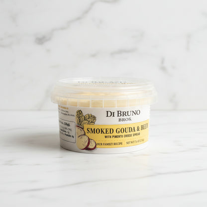 Container of Di Bruno Bros Smoked Gouda & Red Pepper Cheese on a dark surface with a tiled wall background.