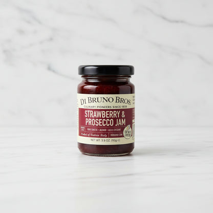 Jar of strawberry and prosecco jam on a black surface with a white background