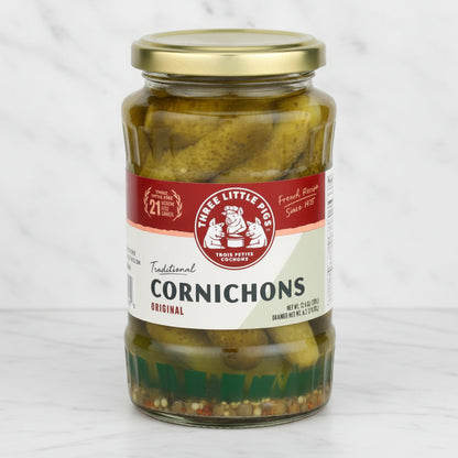 A jar of Three Little Pigs Traditional Cornichons in vinegar, with a label showing the brand logo and the product name.
