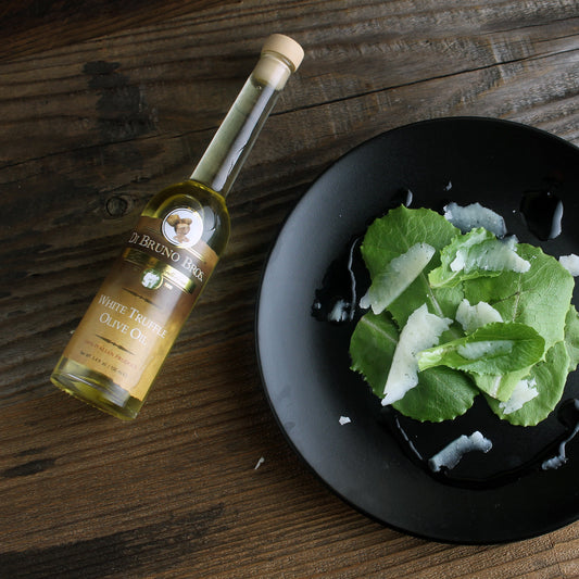 Bottle of olive oil next to a black plate with green salad on a wooden table