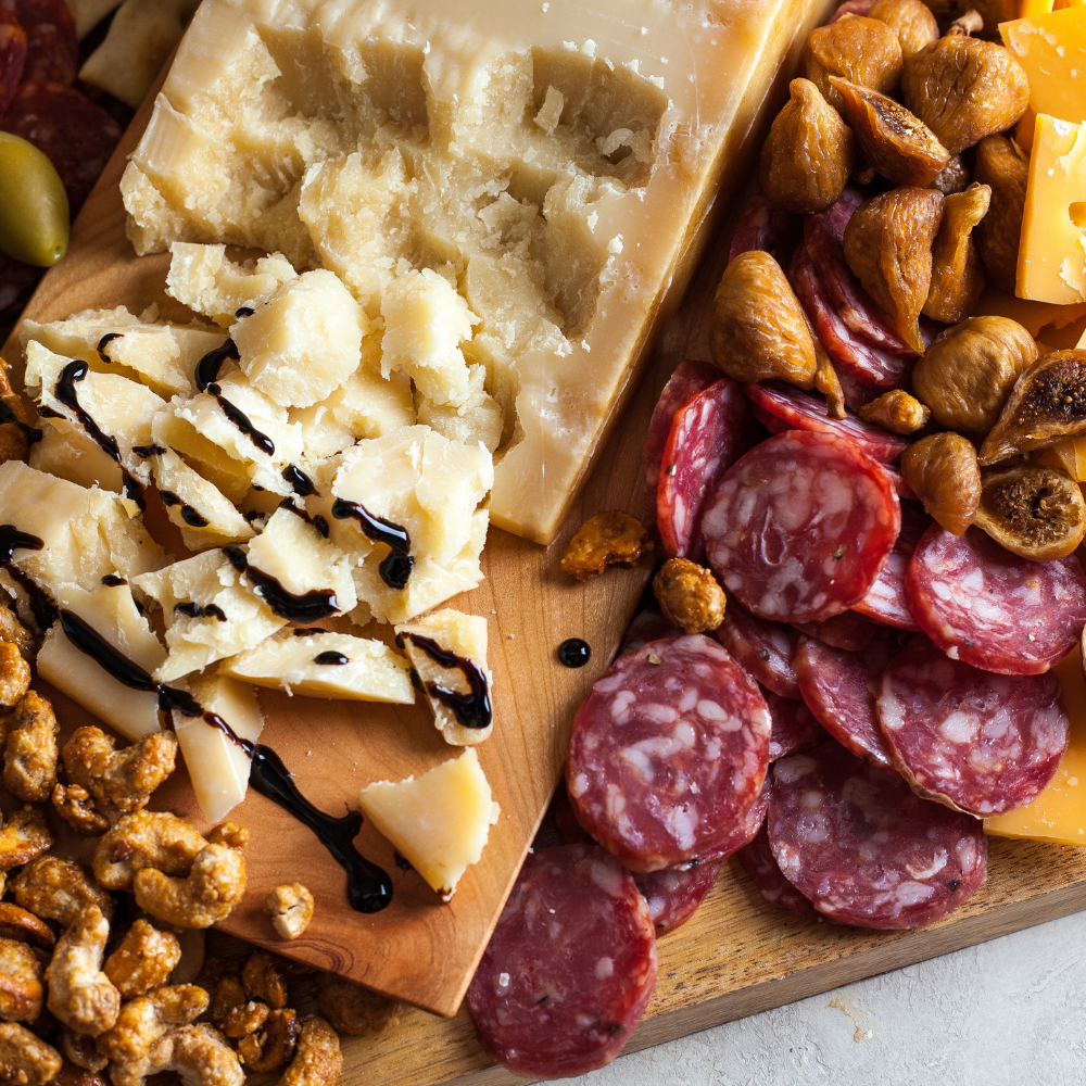 Platter of assorted cheeses, cured meats, and nuts on a wooden board.