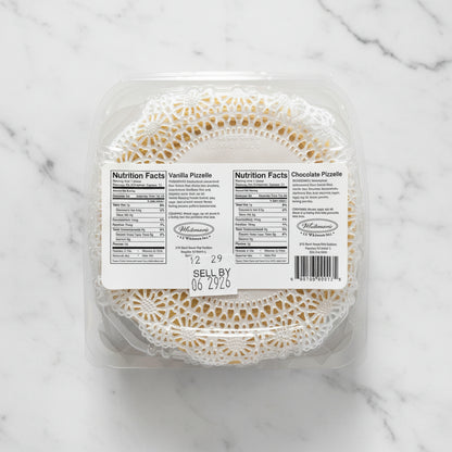 Packaged vanilla and chocolate pizzelles with nutrition labels on a dark surface.