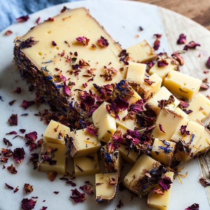 A cheese board featuring a variety of cheeses including a block of Gouda cheese cubes, garnished with dried rose petals.