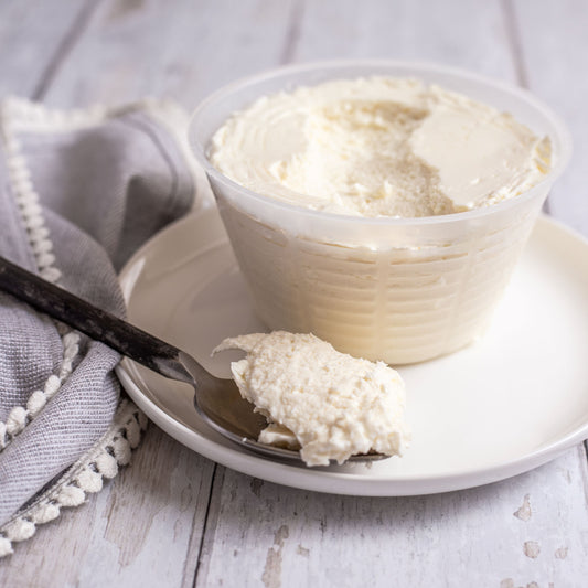 Bowl of ricotta cheese with a spoon on a white plate on a wooden surface