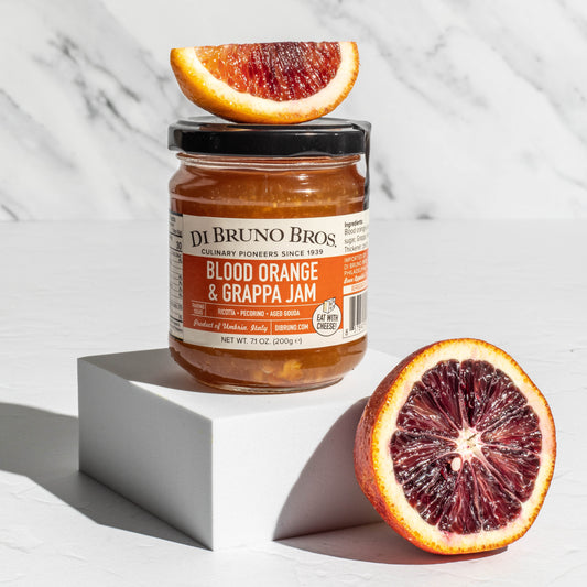 Jar of Di Bruno Bros. Blood Orange & Grappa Jam with blood oranges on a marble background