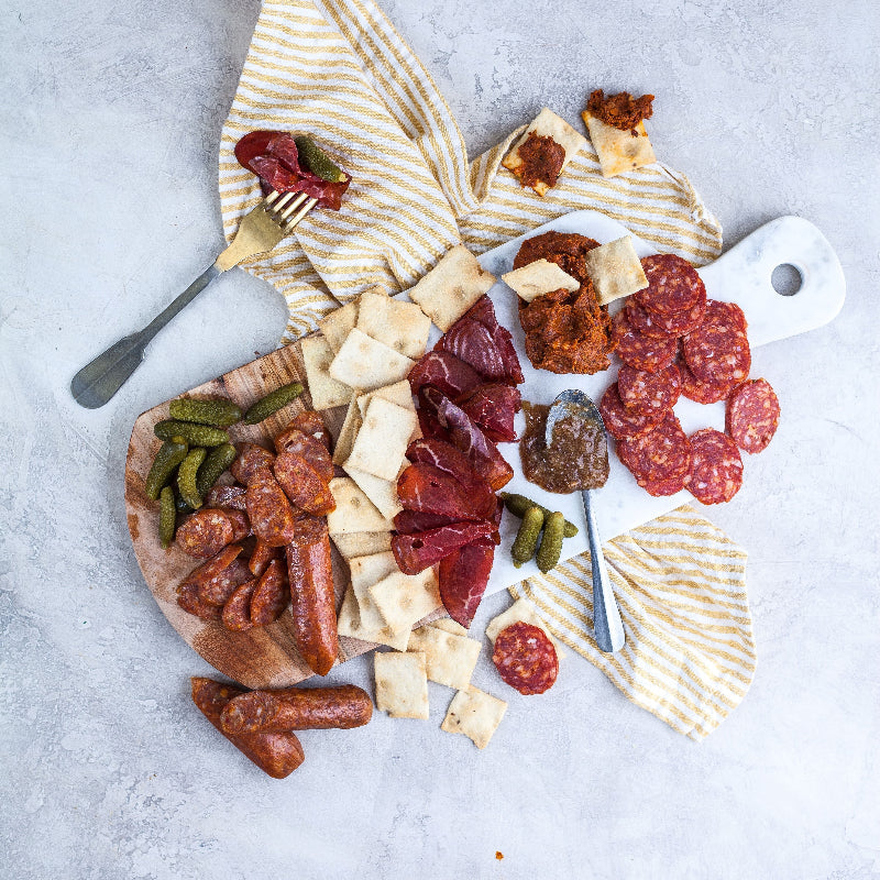 Platter of assorted meats, cheeses, and crackers on a gray surface with a striped towel.