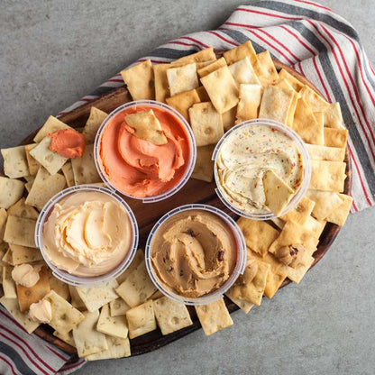 Di Bruno Bros. crostini crackers on a wooden board with four classic cheese spreads in the middle.