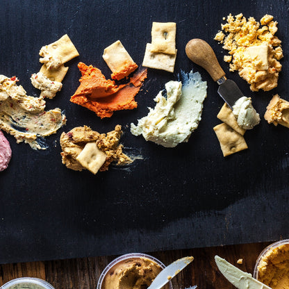 Assorted cheeses and crackers on a dark surface with a knife.