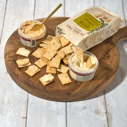 Di Bruno Bros. Crostini Sampler Set is an assortment of flavors including olive oil, parmesan, rosemary, and sea salt, displayed in front of a white background with scattered crostini crackers.