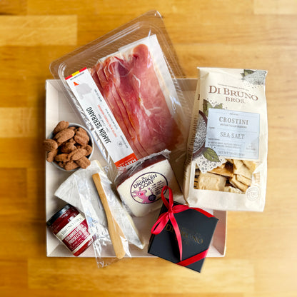 Gift box with meats, cheeses, and other snacks on a wooden surface