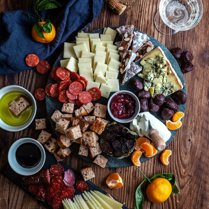 Assorted cheese, crackers, fruits, and meats on a wooden board with glasses of wine.