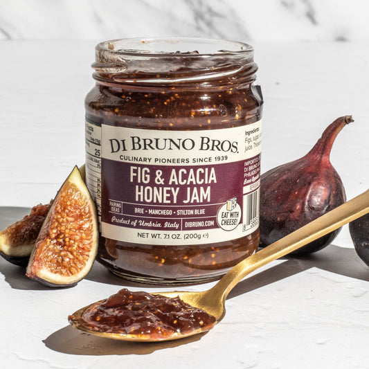 Jar of Di Bruno Bros. Fig & Acacia Honey Jam with figs and a spoon on a white background