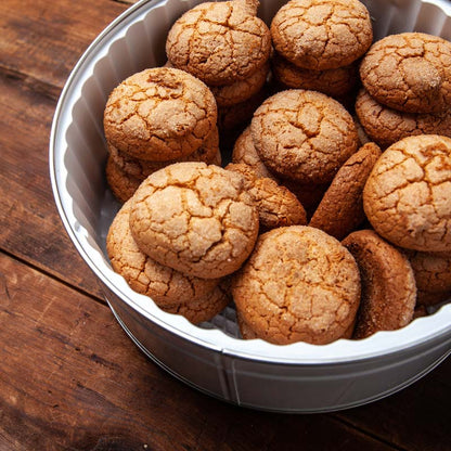 A tin of almond macaroon cookies on a wooden surface.