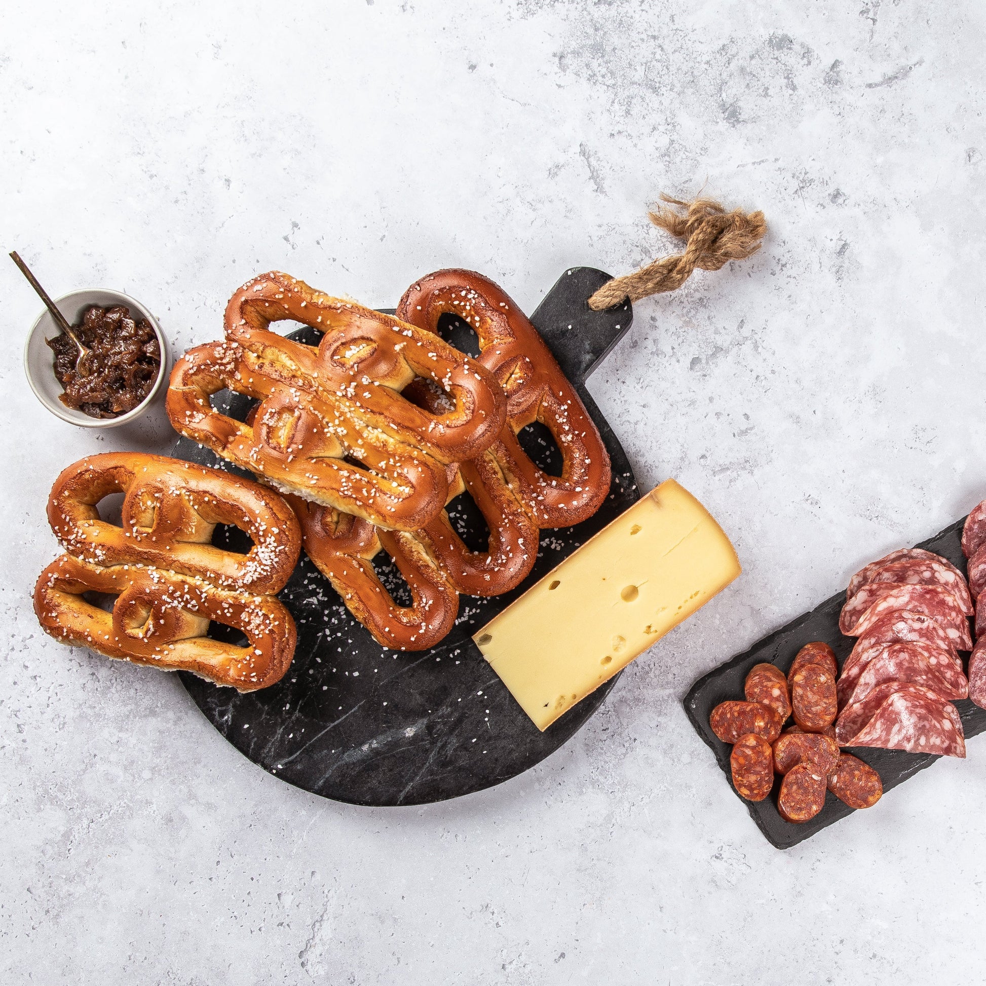 Assorted meats and pretzels on a stone board with a white background