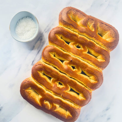 Braided bread loaf on a marble surface with a small bowl of salt.