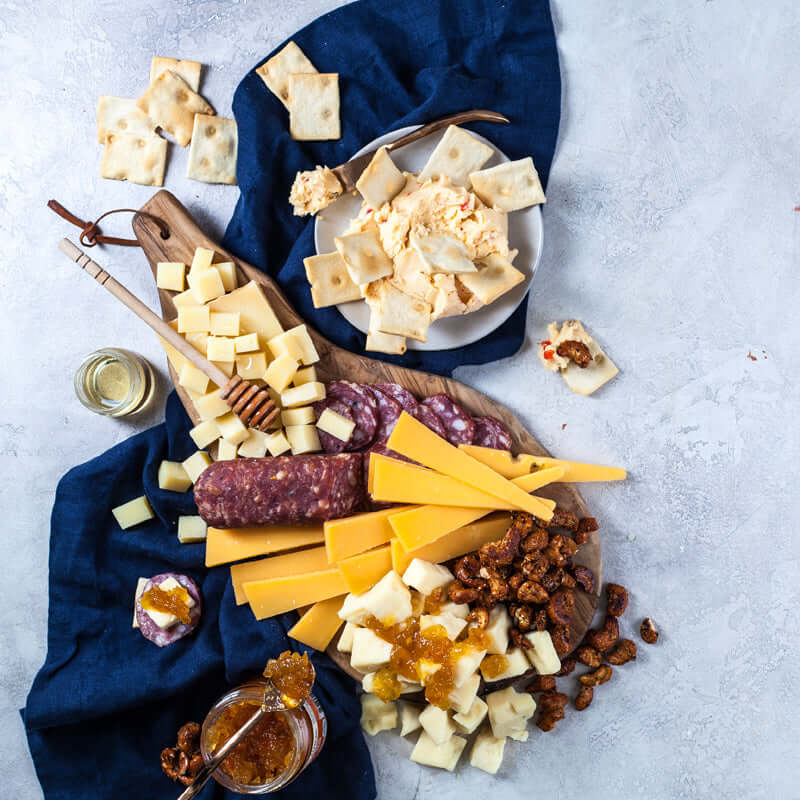 Overhead serving suggestion with cheeses, sliced salami, crostini, cheese spread, honey, jam, and candied nuts