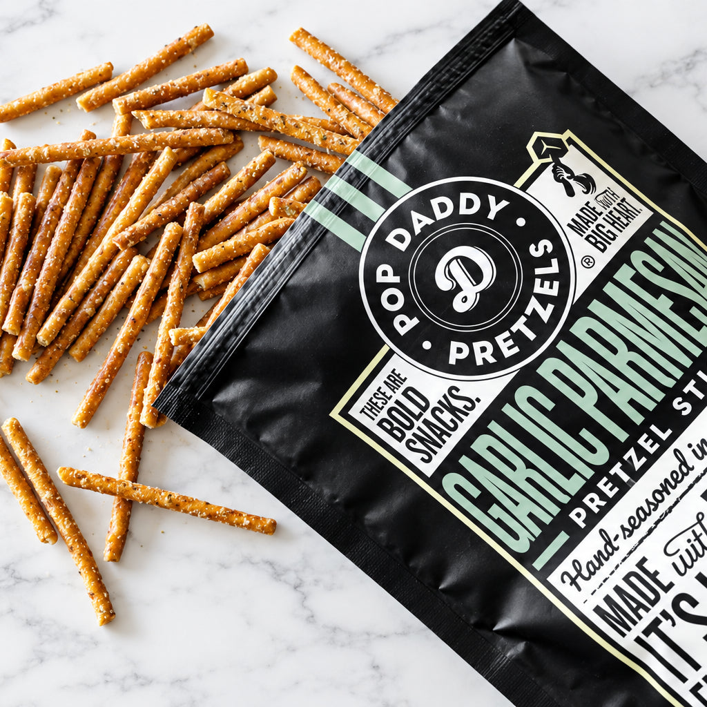 A bag of Pop Daddy Pretzels Garlic Parmesan flavor with pretzels spilled out on a white wood background.