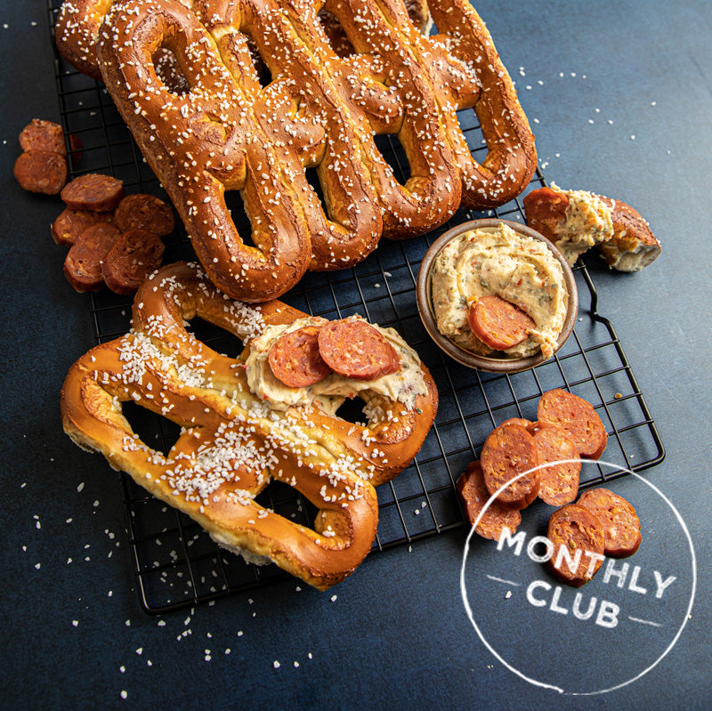 A photo of a freshly made soft pretzel with a side of mustard, on a cooling rack.