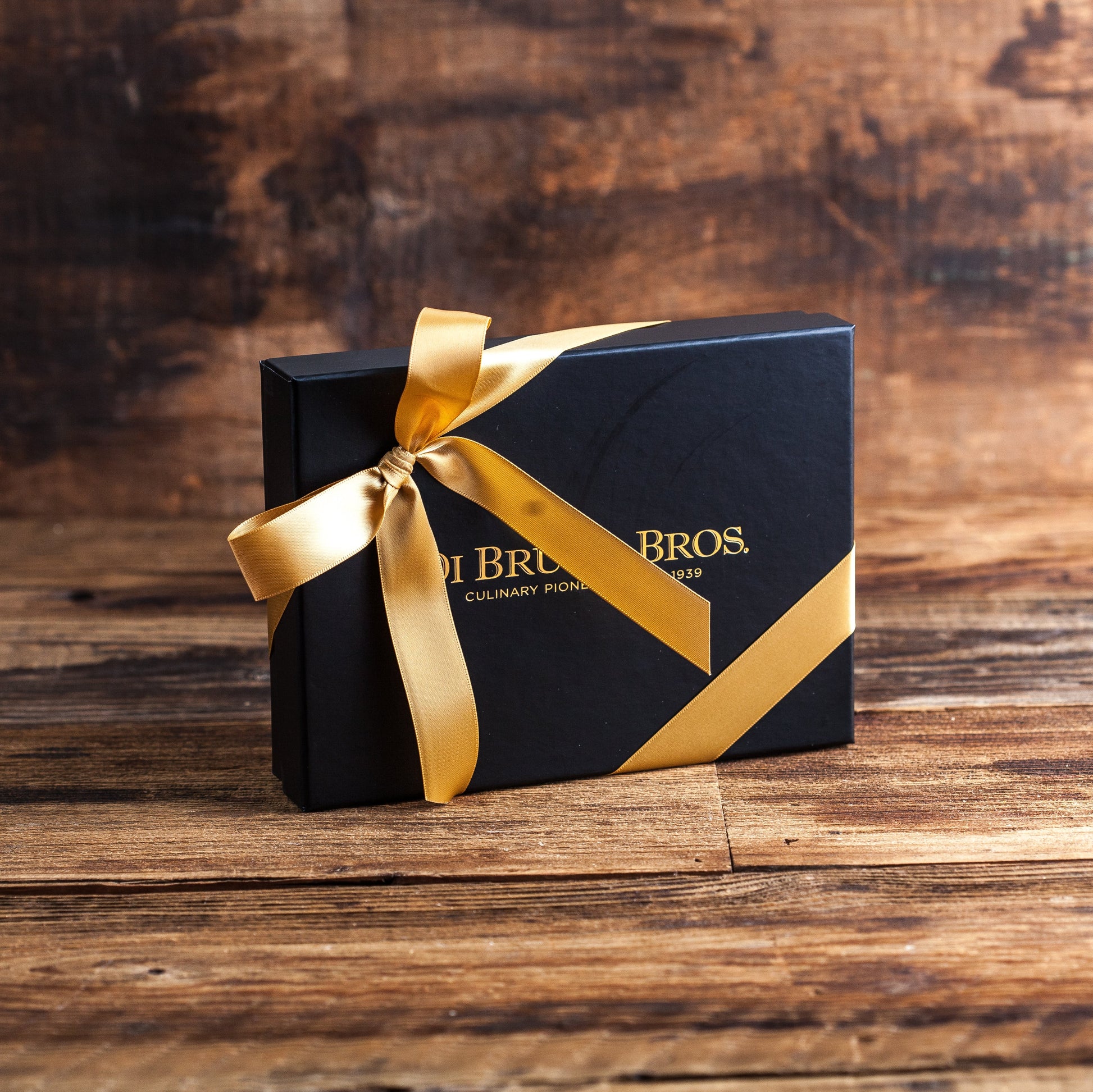 Black gift box with gold ribbon and 'Brisa & Bros' branding on a wooden surface
