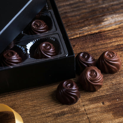 Chocolate truffles in a black box on a wooden surface with a red ribbon.