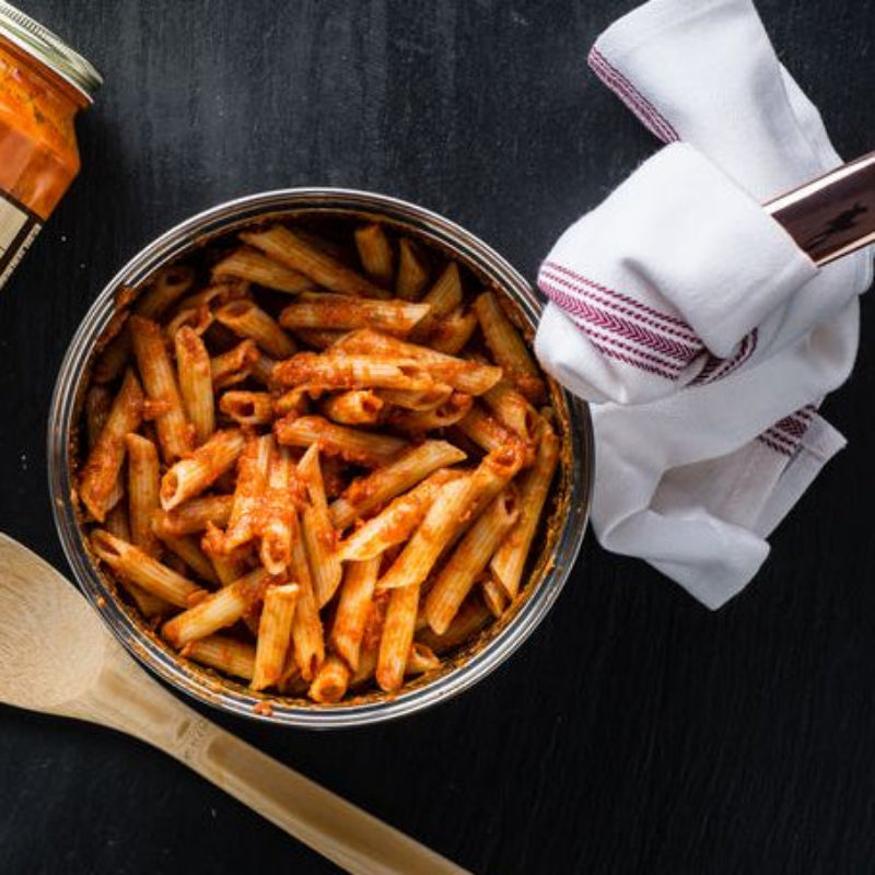 Bowl of pasta with a jar of sauce and wooden spoon on a black surface