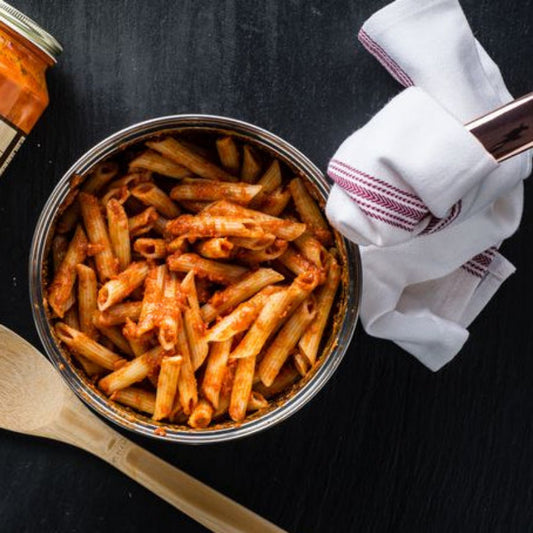 Bowl of pasta with a jar of sauce and wooden spoon on a black surface