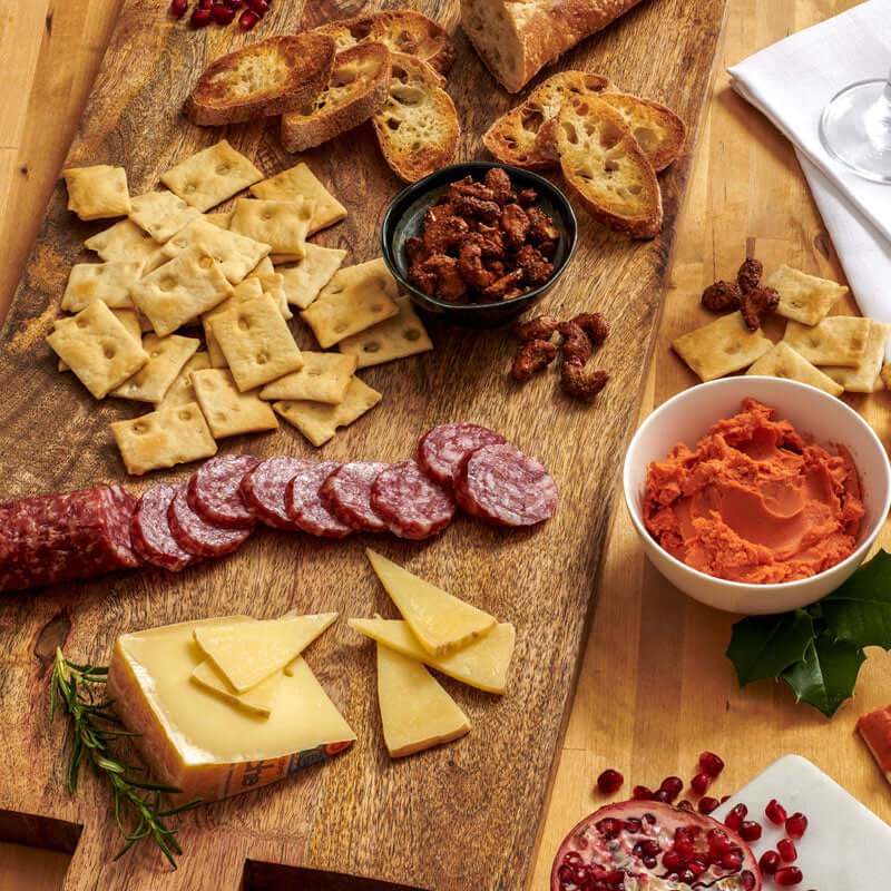 Taste of Di Bruno cheese and charcuterie serving display with salami, Manchego, crostini, cheese spread, and candied nuts