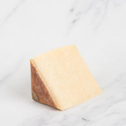 A wedge of Traversetolese White Gold Parmigiano Reggiano cheese on a marble surface.
